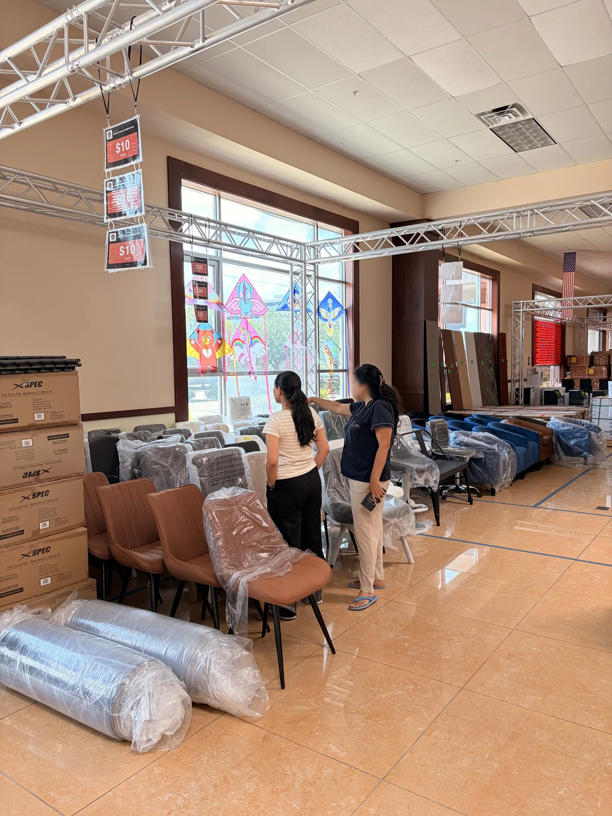 Two shoppers looking over rows of wrapped chairs beneath hanging ten dollar signs
