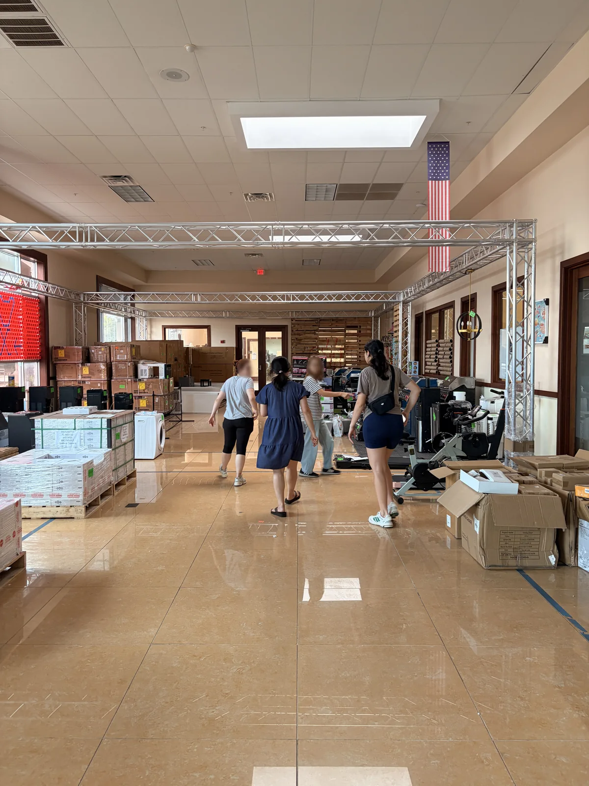 Shoppers walking the main aisle of the Cube-Age Houston sale floor past appliances and fitness gear
