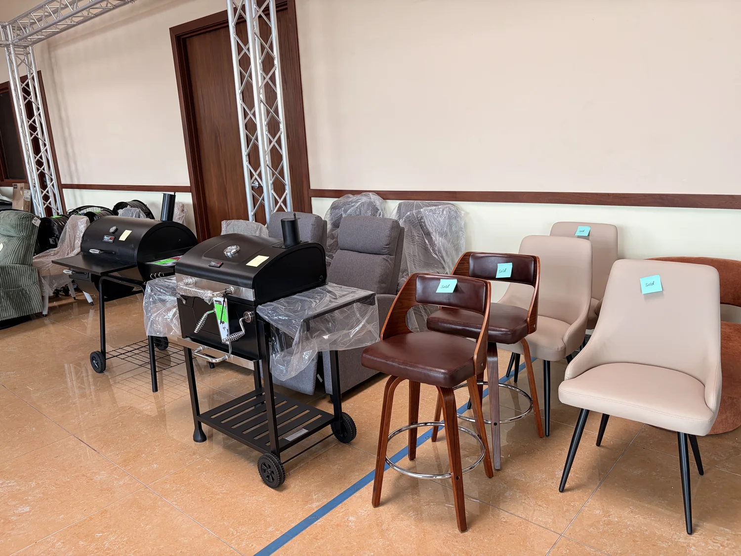 Charcoal grills and upholstered chairs on the Cube-Age Houston floor, several marked with handwritten Sold tags