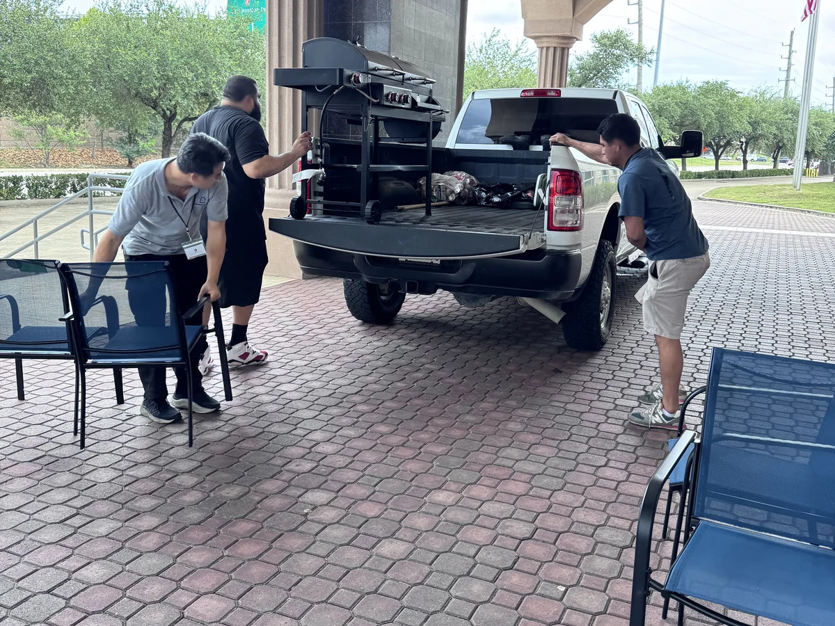 Three people lifting a griddle cart into a pickup at the Cube-Age Houston sale