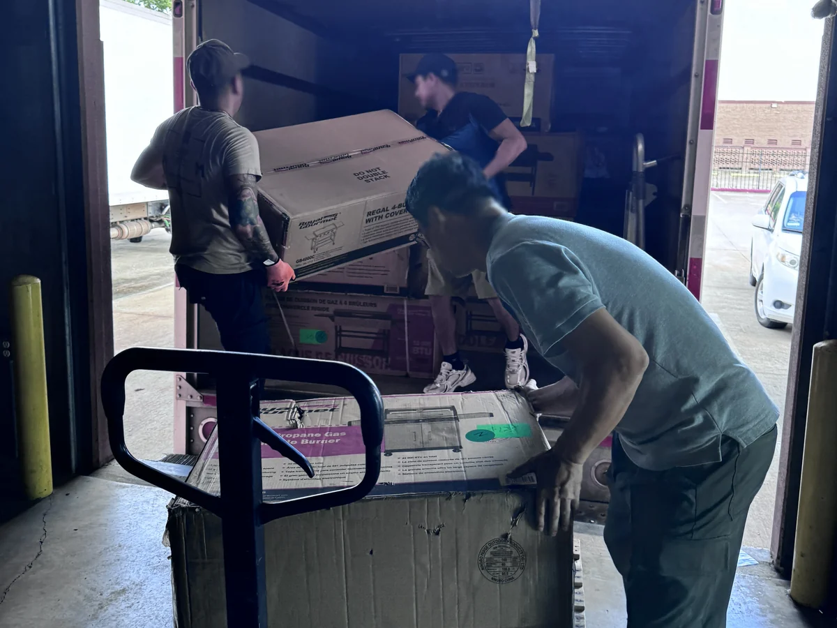 Loading price-tagged boxed grills into a wholesale buyer box truck at the Cube-Age Houston sale