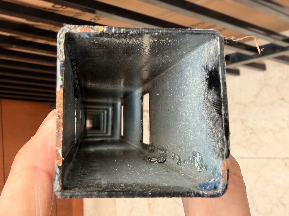 Looking down the inside of a fence rail: bare grey steel with no coating