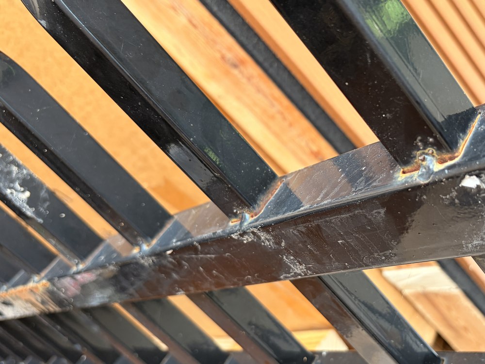 A stack of new powder-coated fence panels still in cardboard, showing rust along the rails