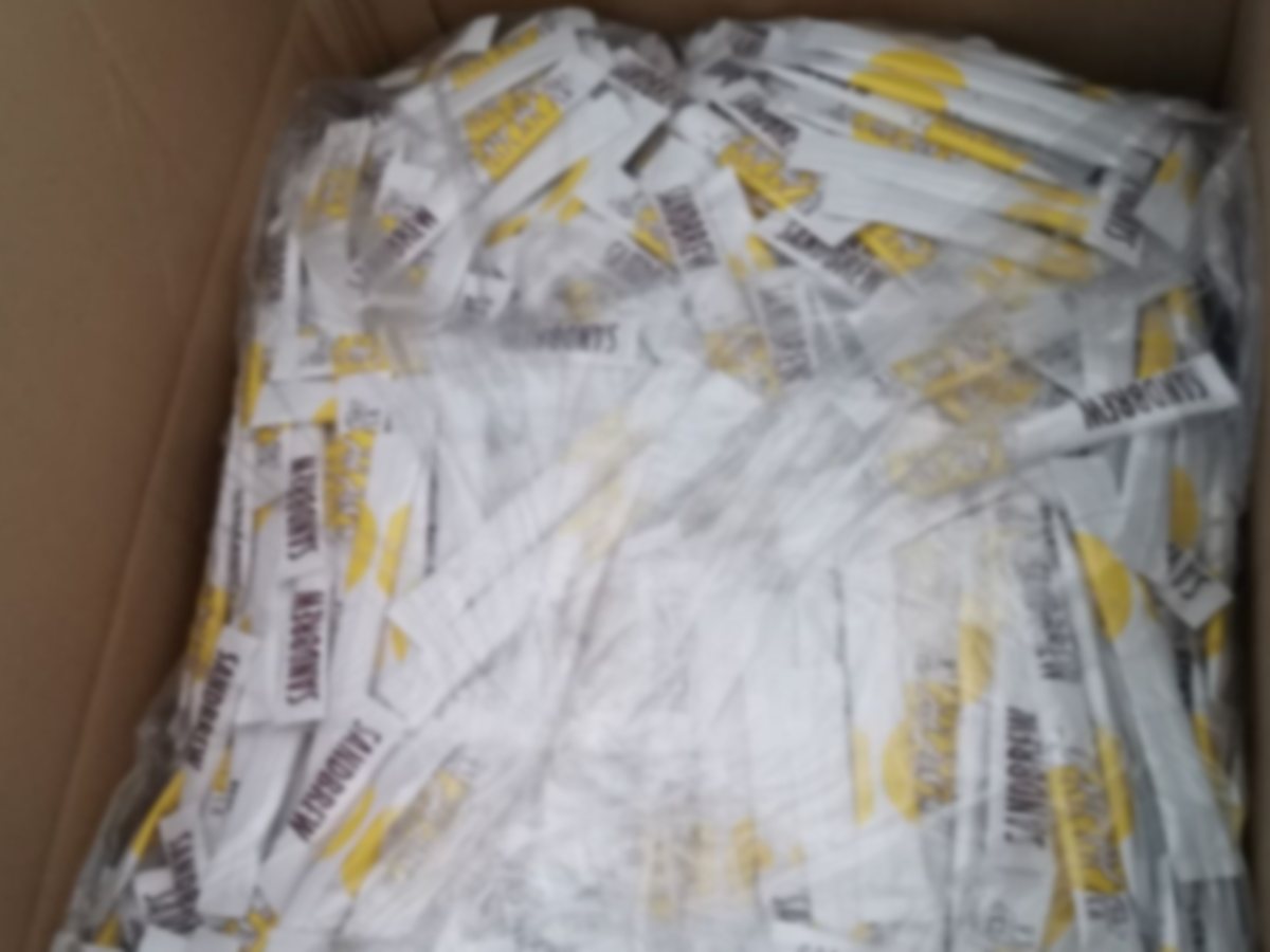 A carton of individually wrapped white cane sugar sticks as it arrives